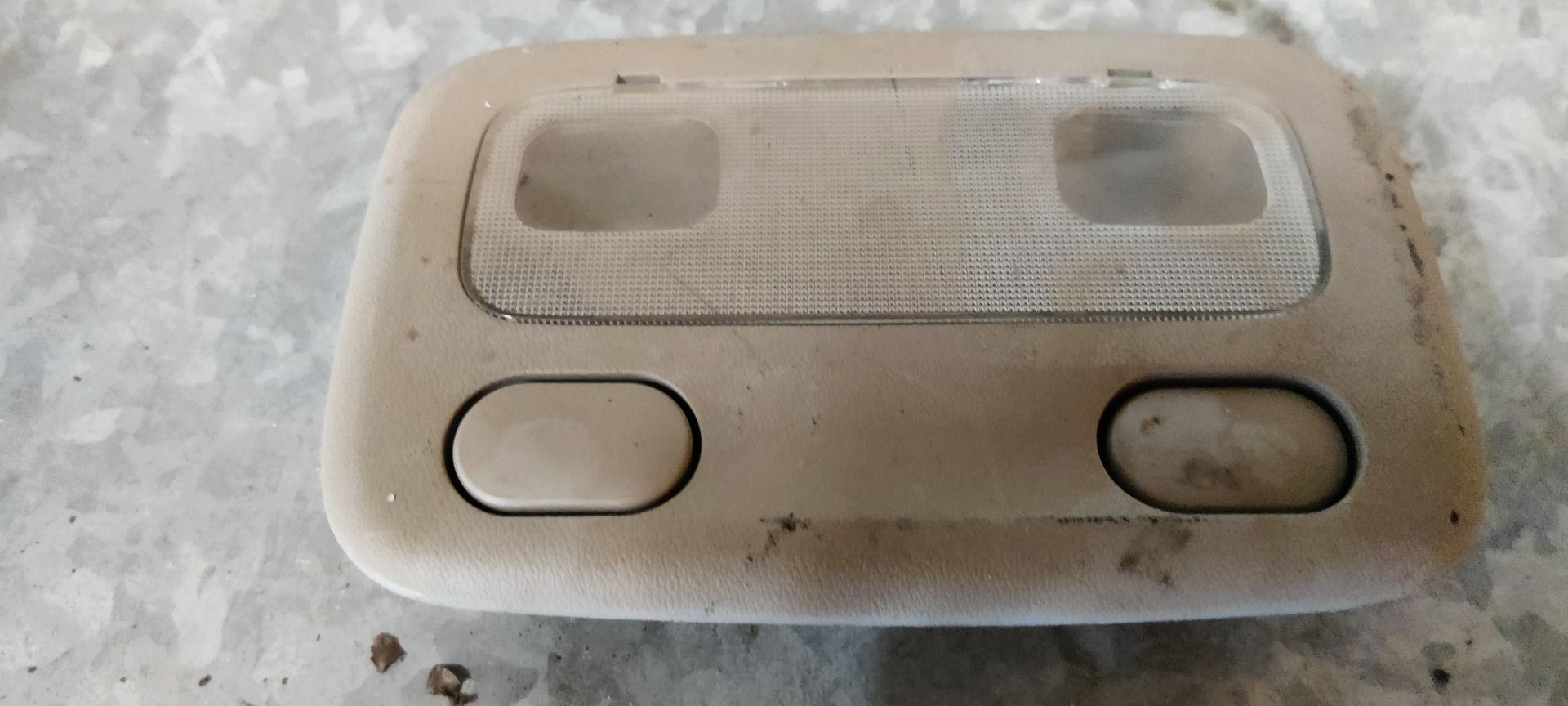 Een beige interieurverlichtingsunit voor auto's met twee knoppen en een transparante plastic lens, van bovenaf gezien.