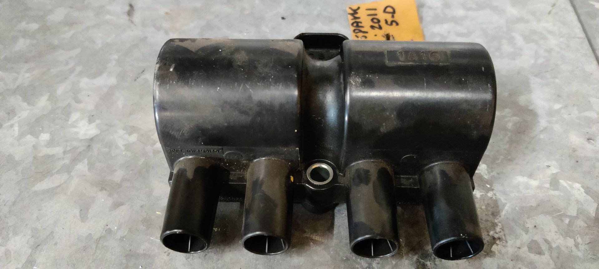 Een zwarte bobine voor een Chevrolet Spark uit 2011, met vier aansluitingen voor bougiekabels en een geel identificatielabel.