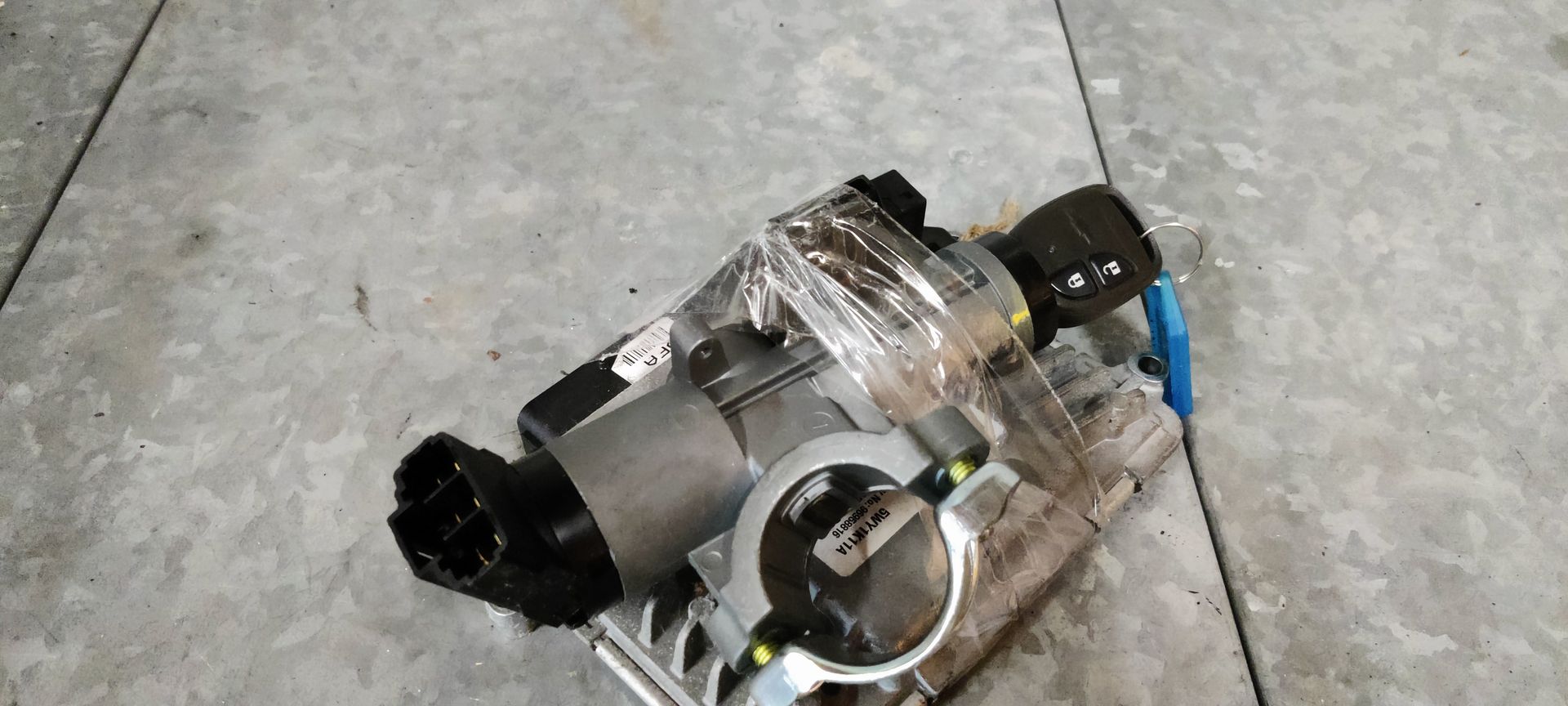 Een elektronisch gasklephuisonderdeel met elektrische aansluitingen, dat op een grijze tegelvloer ligt.