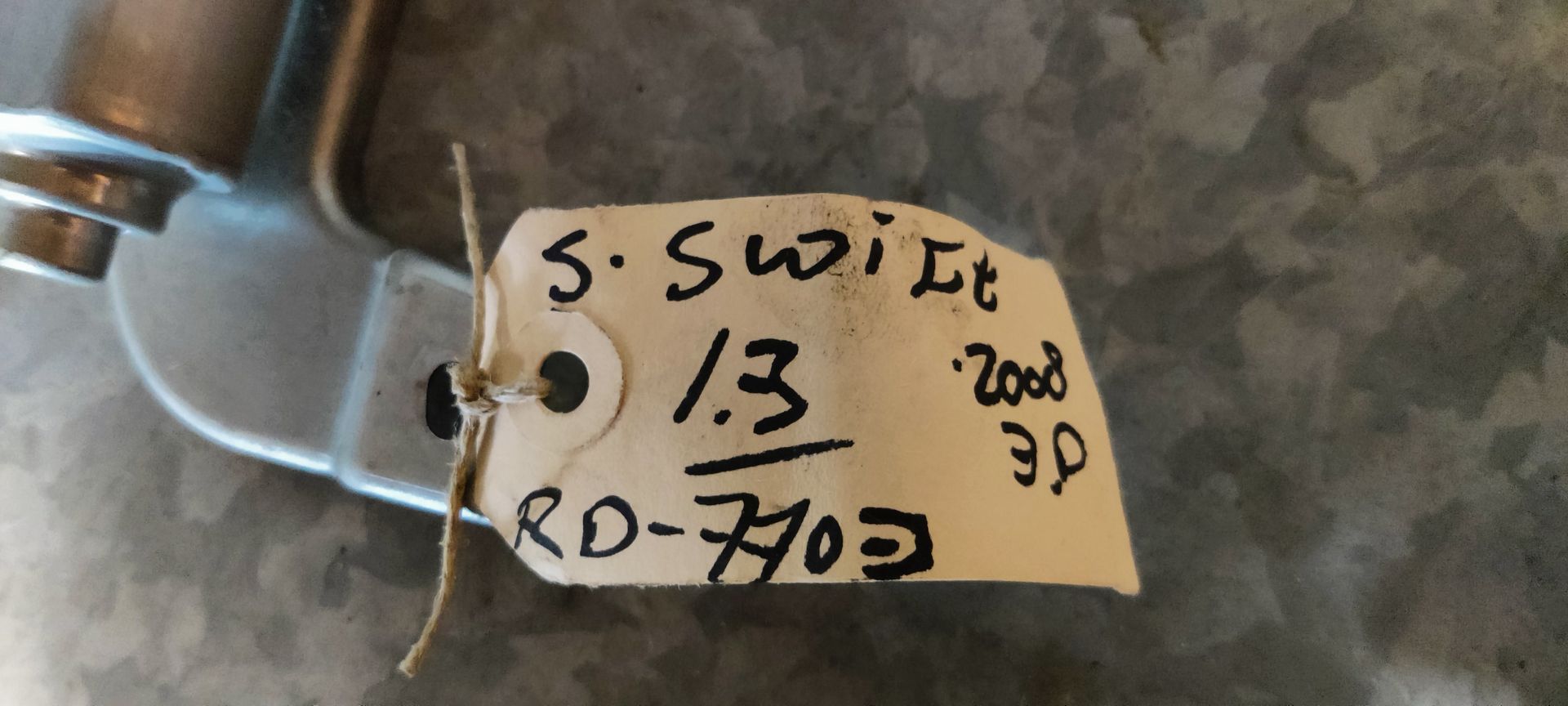Een metalen raammotor voor een auto, met een zwart plastic tandwiel, rustend op een grijze tegelondergrond.