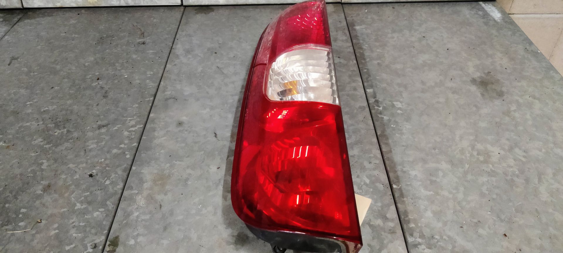 Een rode en transparante achterlichtunit van een auto, van de zijkant gezien, rustend op een grijze betonnen ondergrond.