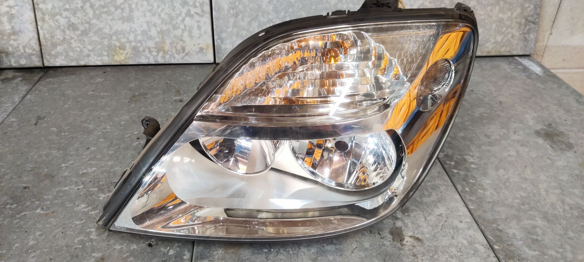 Een enkele autokoplampunit met een heldere lens, verchroomde interne reflectoren en een oranje zijmarkeringslicht.