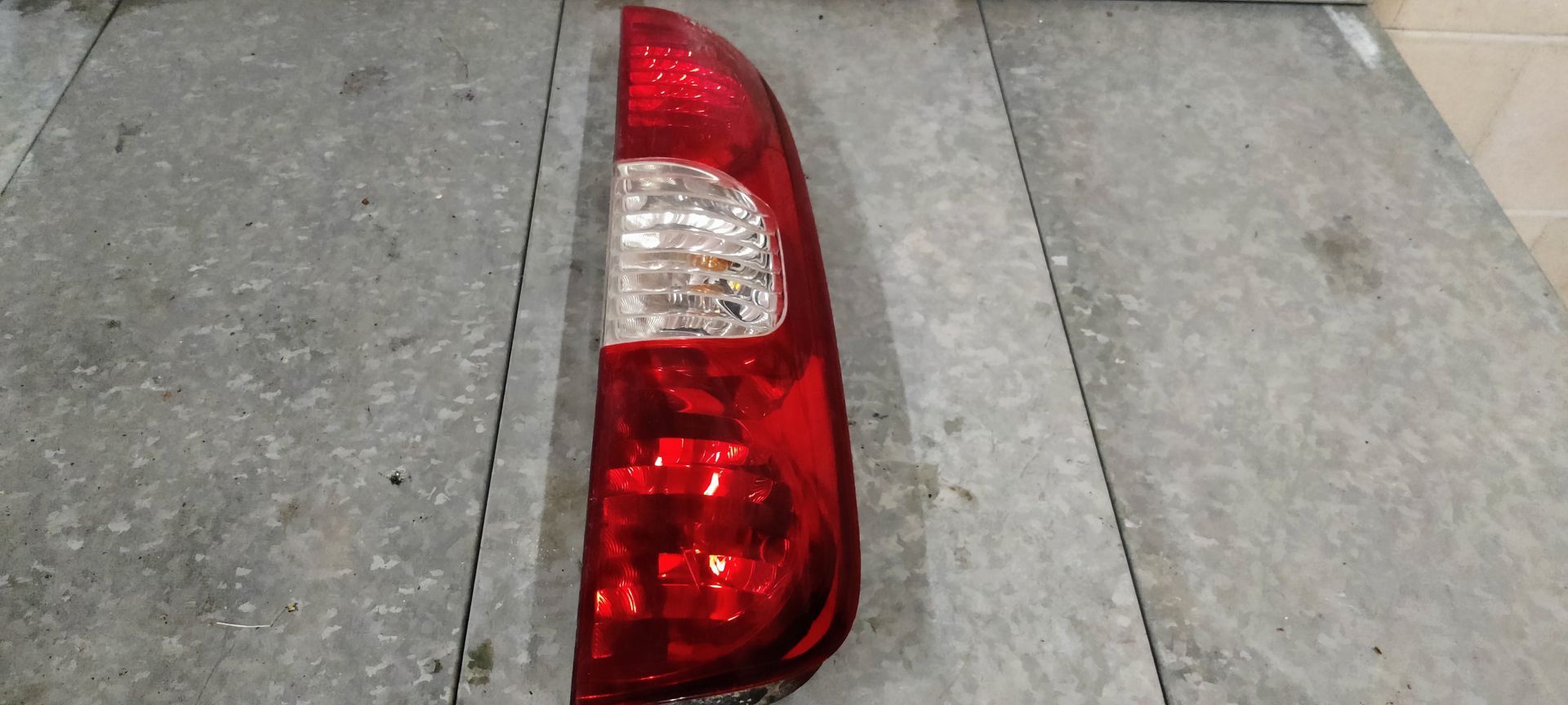 Een rode en transparante autoachterlichtunit, verticaal geplaatst op een grijze ondergrond.