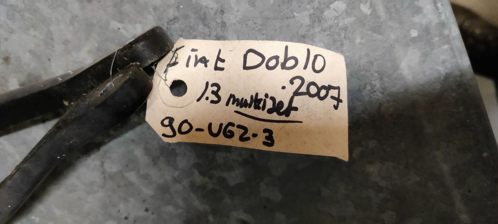 Drie versleten, zwarte ruitenwisserbladen van een auto liggen op een lichtgrijze tegelvloer.