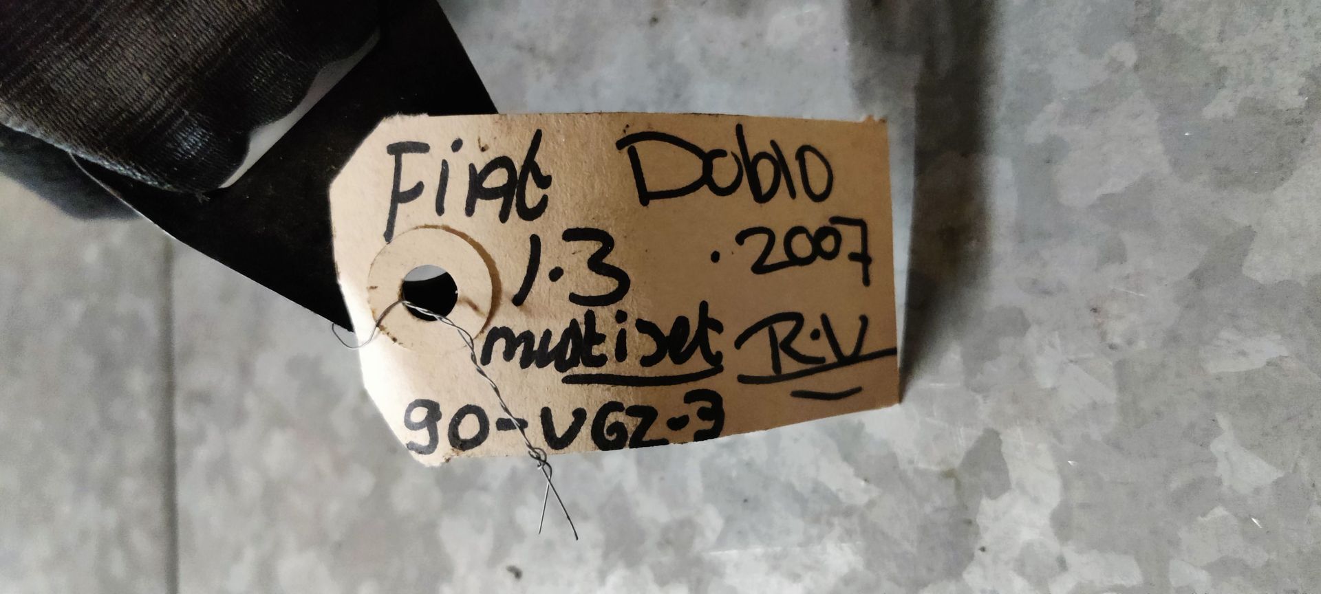 Een oprolmechanisme voor een autogordel, omwikkeld met beige tape, ligt op een grijze vloer met een identificatielabel eraan.