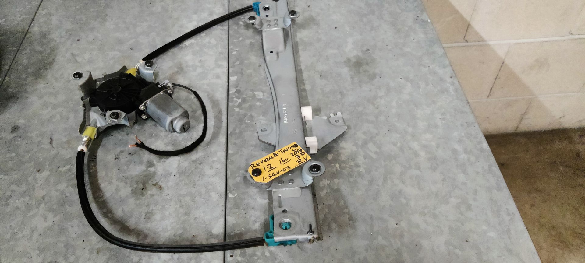 Een raammechanisme voor een auto met een aangehechte motor op een grijze ondergrond met een geel label.