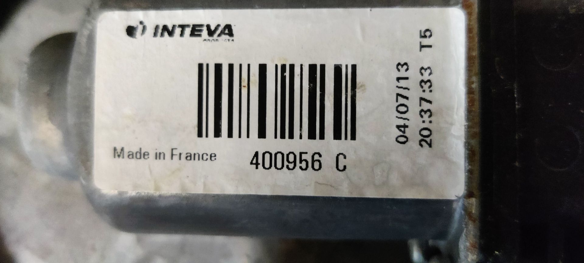 Een raammechanisme voor een auto met een aangehechte motor op een grijze ondergrond met een geel label.