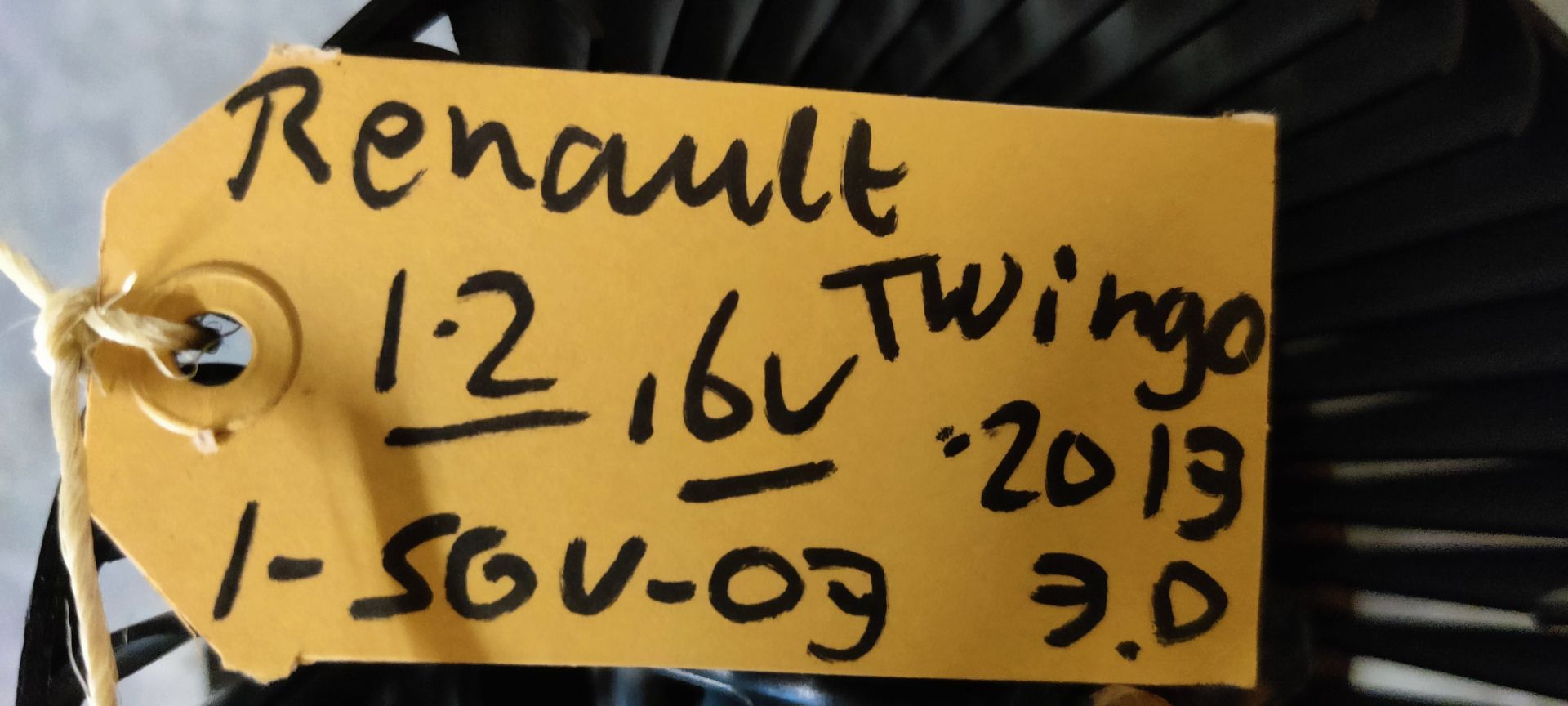 Een zwarte ventilator voor een airconditioningsysteem in een auto, met een ventilatorbehuizing, staat op een grijze vloer.