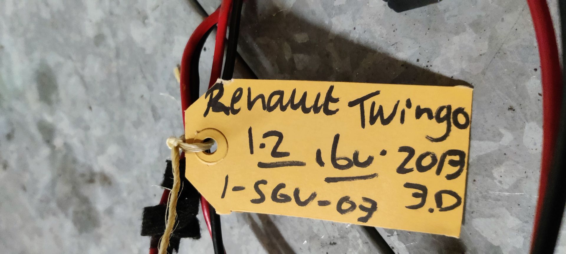 Een weerstand van een autoventilator met kabelboom en plastic connector, rustend op een grijze tegelondergrond.