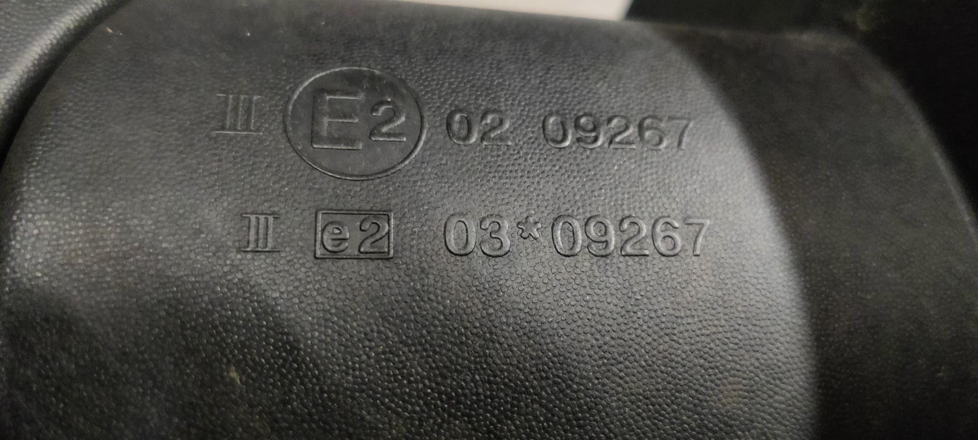 Zwarte zijspiegel van een auto met een geel identificatielabel, rustend op een grijze betonnen vloer.