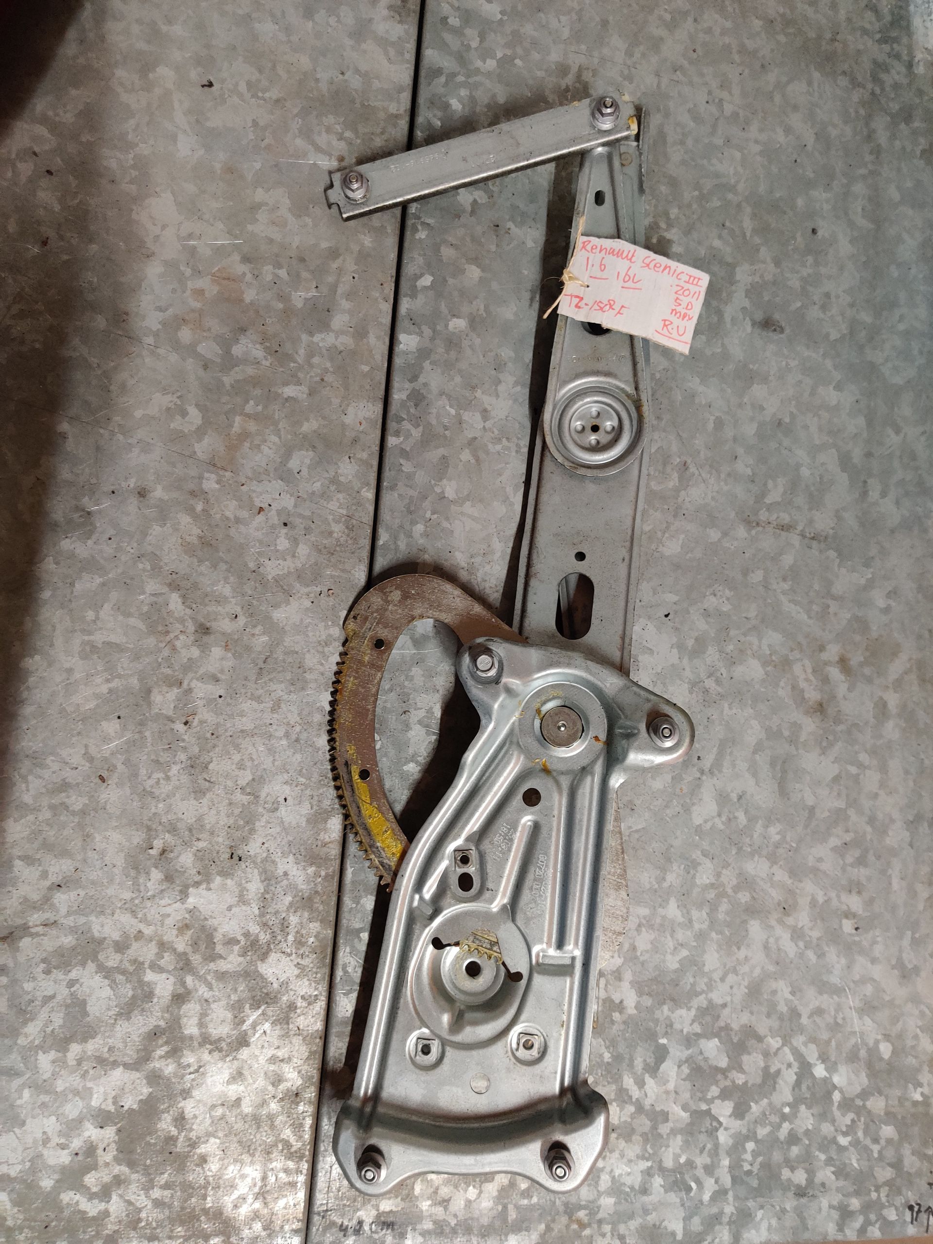Metalen mechanische constructie met een kabel en label op een grijze betonnen vloer.
