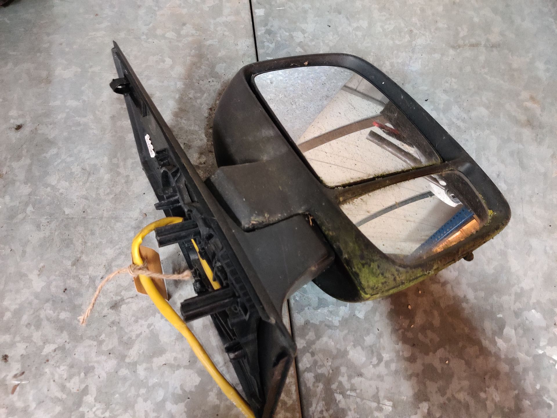 Een Fiat Scudo autospiegel ligt op een betonnen vloer, met blootliggende gele draden.