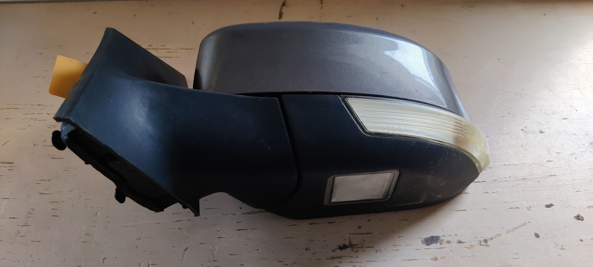 Ford Focus. Een zwarte autospiegel met een klein identificatielabeltje aan de bevestigingsvoet.