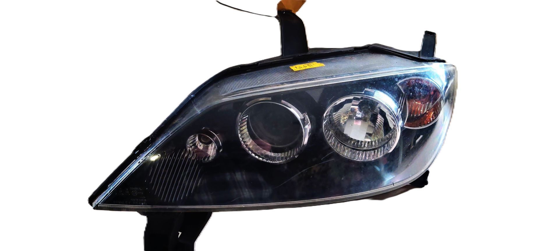 Een zwarte autokoplampunit met ronde projectorlenzen en een transparante behuizing, afgebeeld tegen een witte achtergrond.