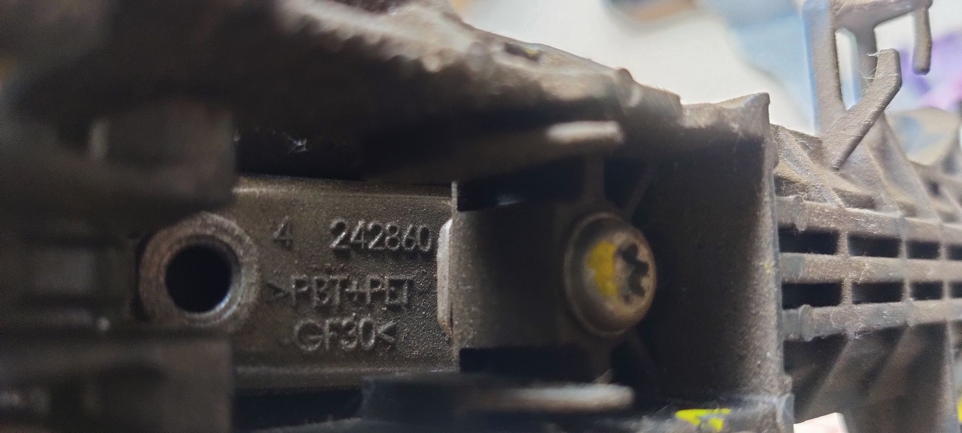 Een grijze buitendeurhendel voor een Toyota Yaris met een aangehecht identificatielabel.