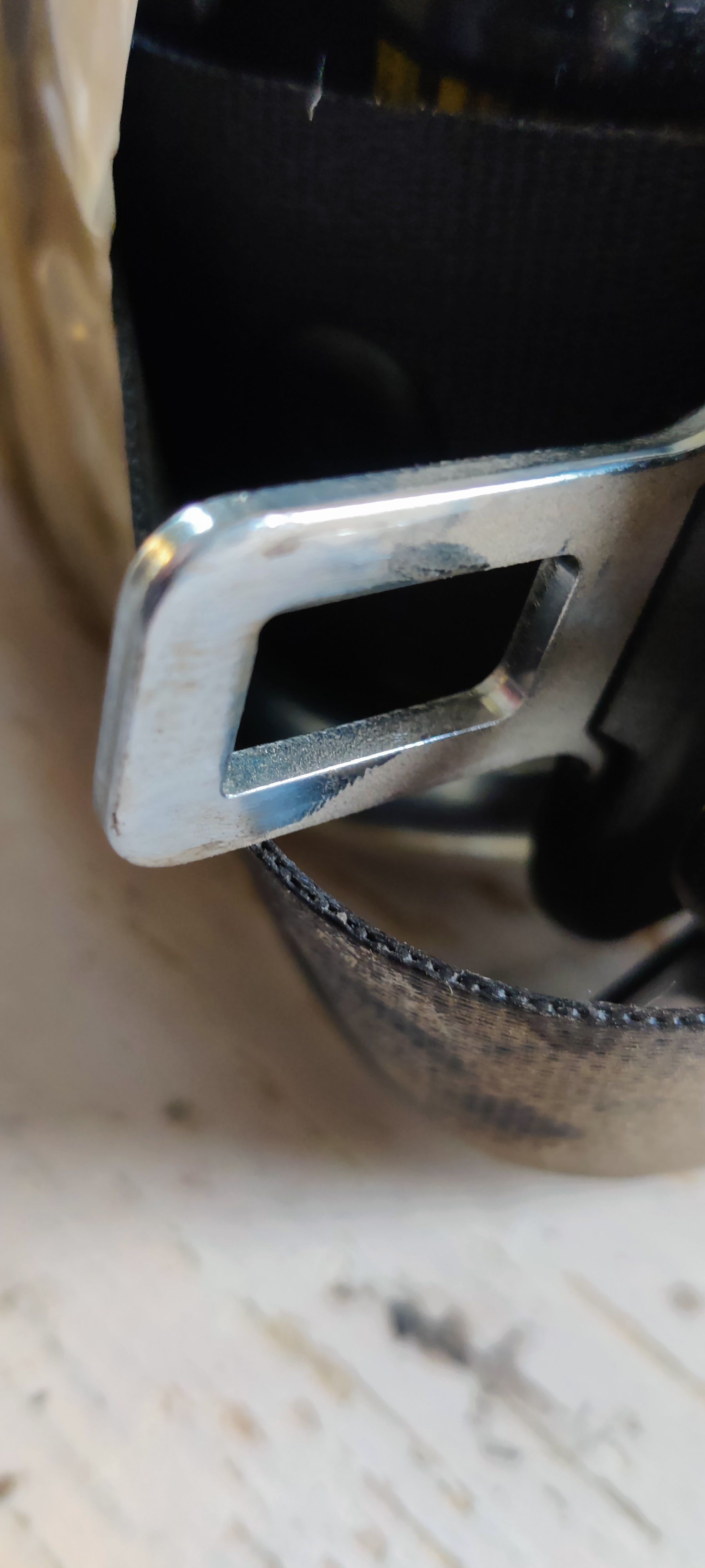 Een zwart gordelspannermechanisme, vastgezet met een strook beige plakband, met daarop een klein blauw plastic onderdeel.