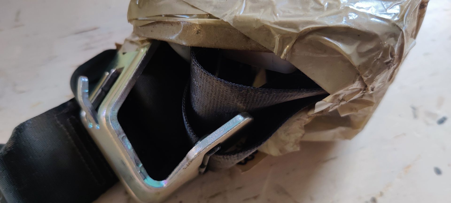 Een autogordelgesp, verpakt in beschermend bruin papier en tape.