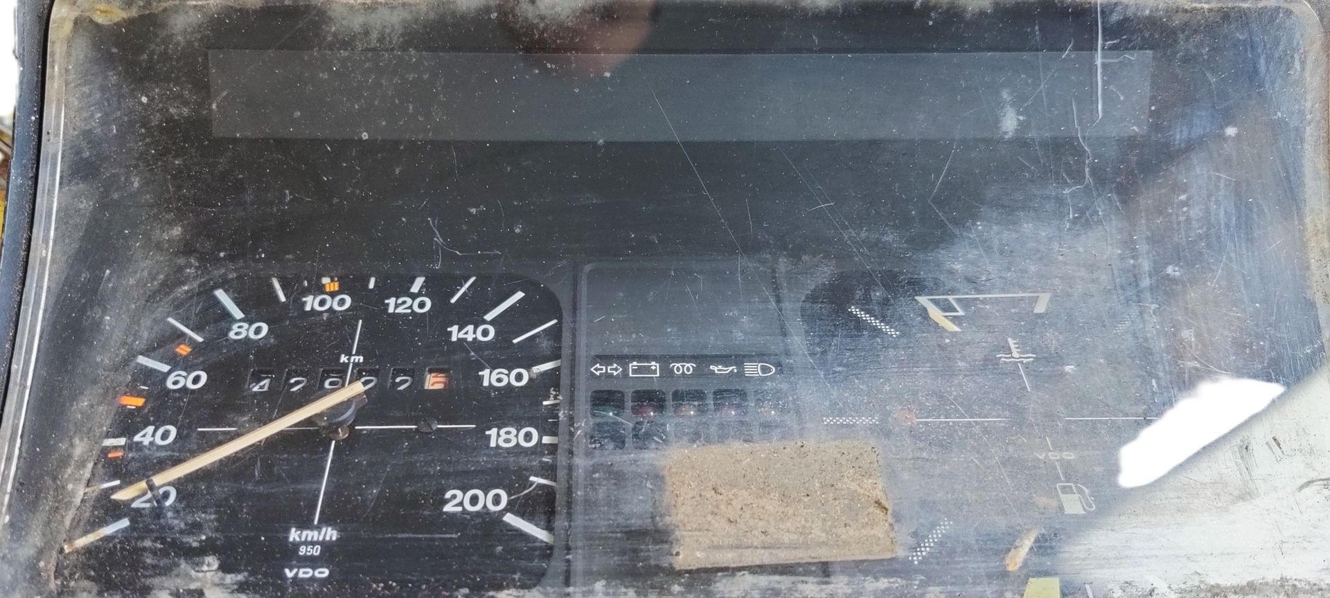 Een stoffige, vintage snelheidsmeter en brandstofmeter met een zwart dashboard en witte markeringen.