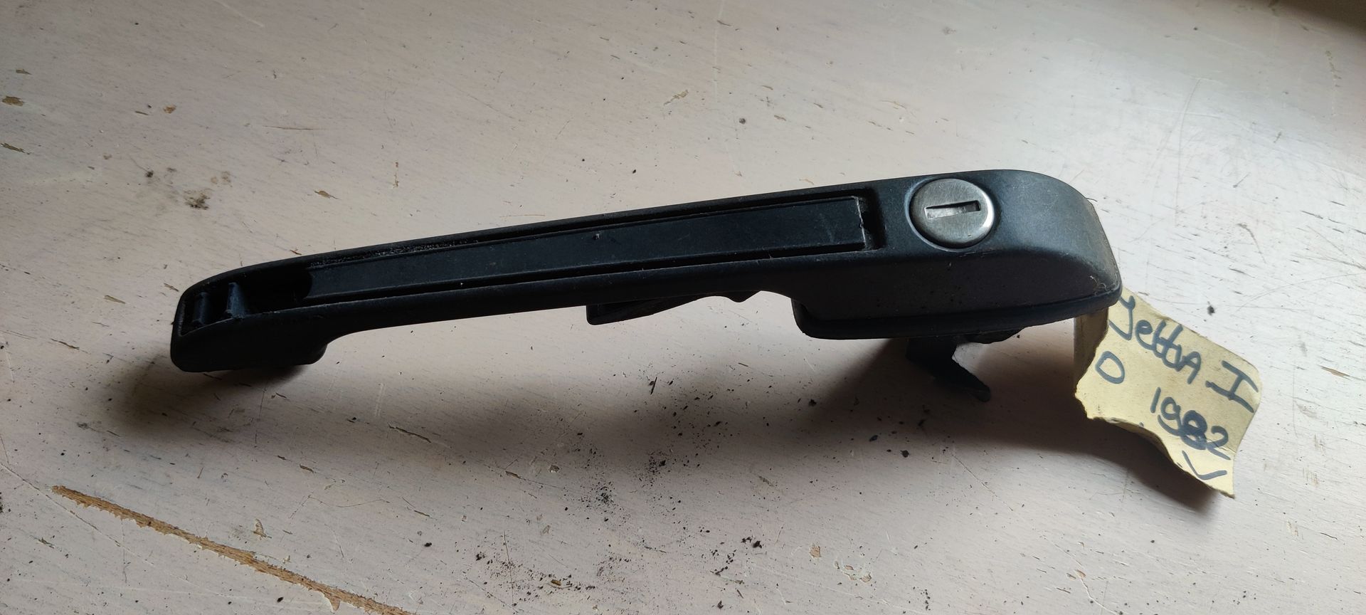 Een zwarte buitendeurhendel voor auto's met een ingebouwd slotcilinder, voorzien van een papieren identificatielabel.