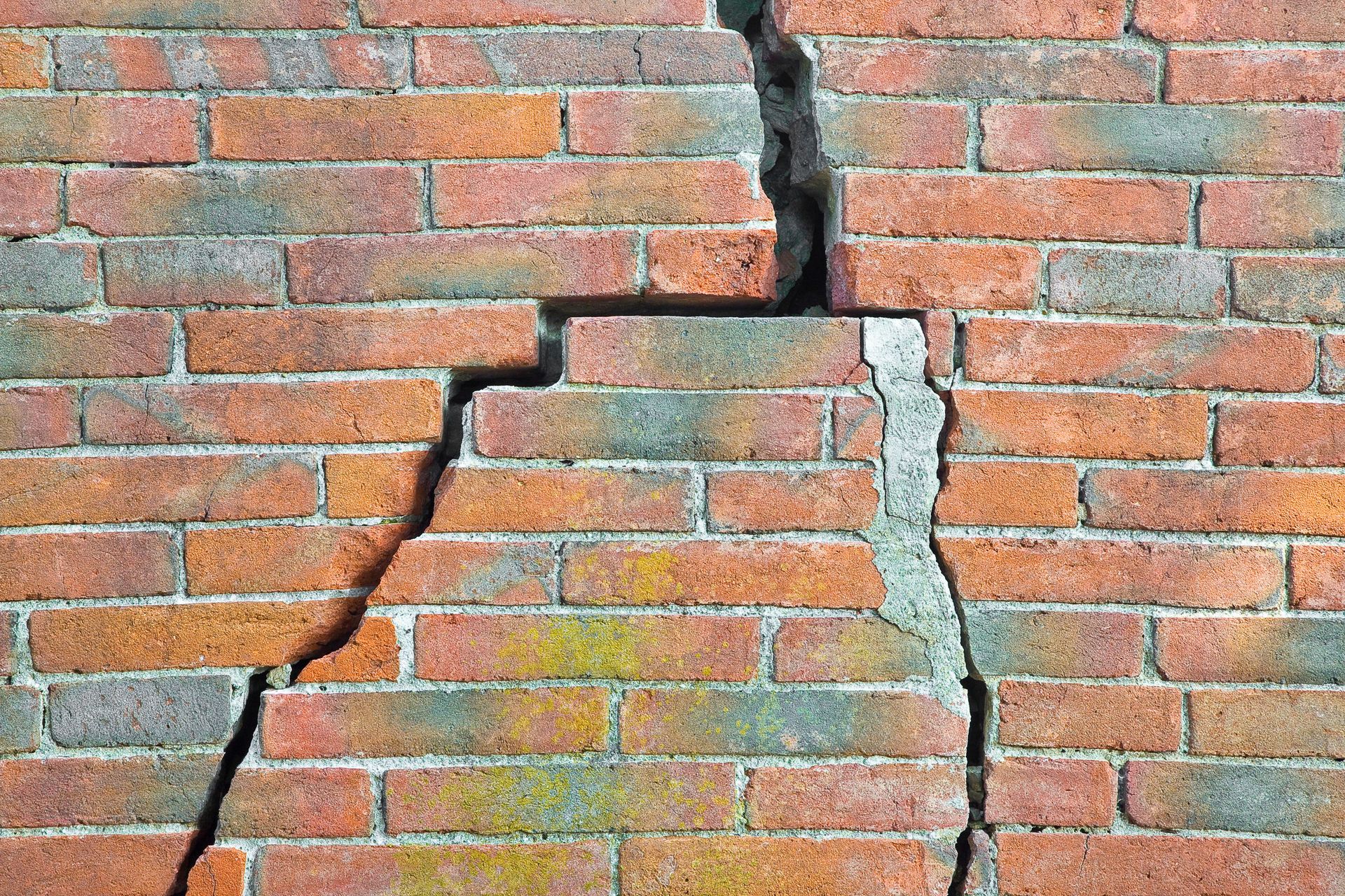 Cracked brick wall with a large vertical and diagonal fracture running through the center