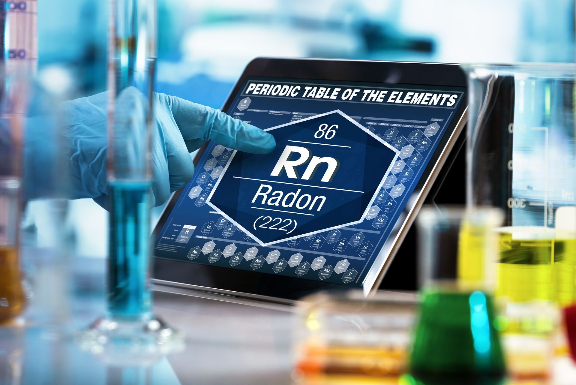 Periodic table tile for radon (Rn) on a lab bench, surrounded by glassware and colorful test tubes