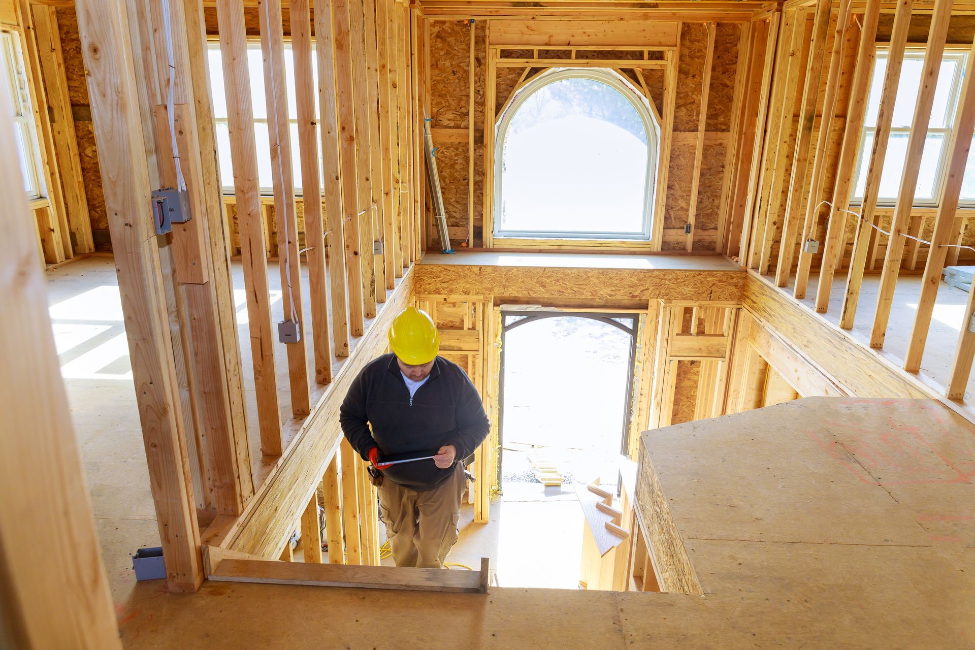 Worker in a hard hat inside a wood-framed house under construction, seen from an upstairs landing