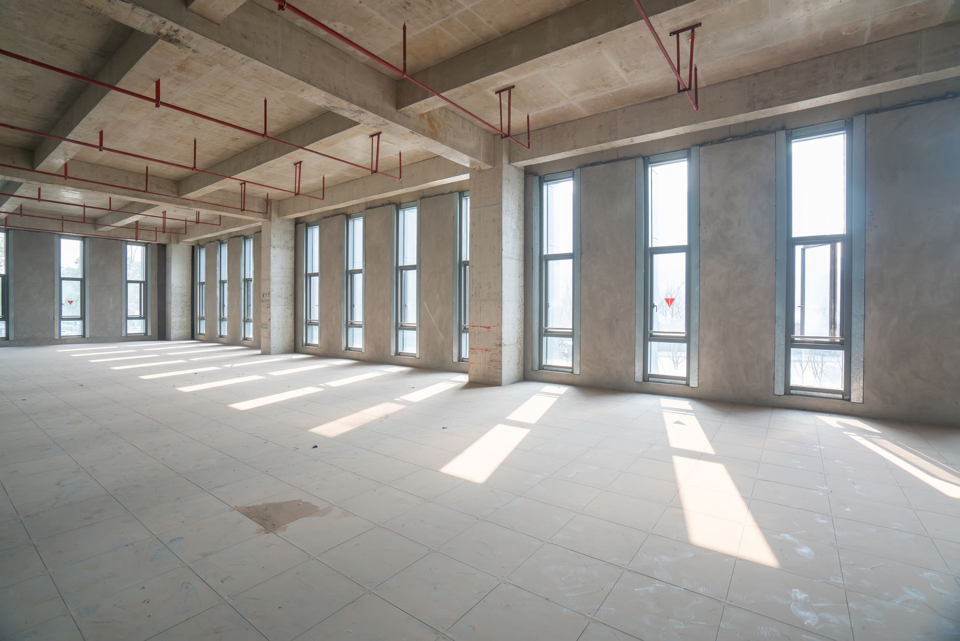 Empty unfinished concrete room with large windows and sunlight streaming onto the floor