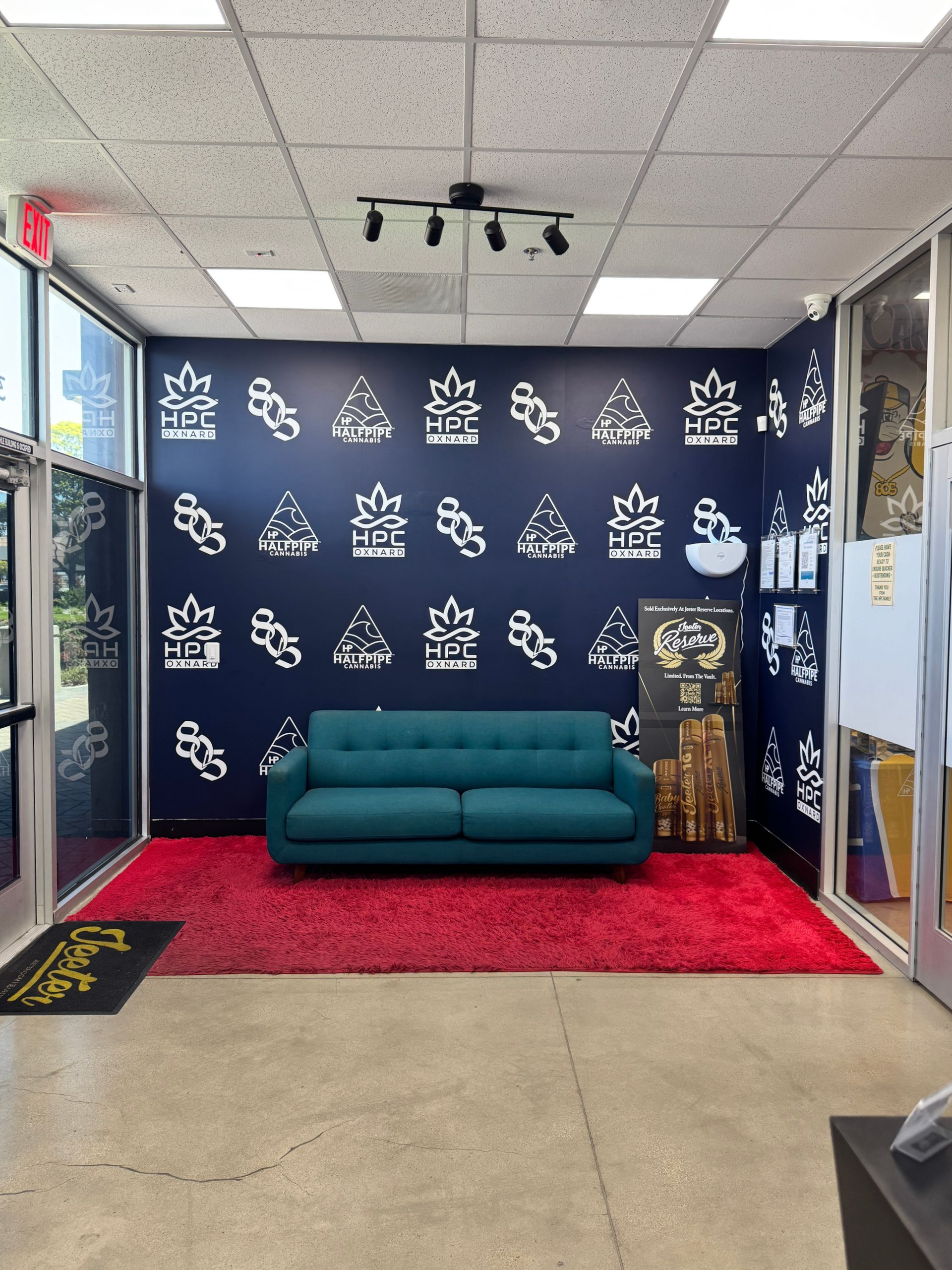 Teal couch on a red rug in a small lobby with dark blue branded wall and ceiling track lights