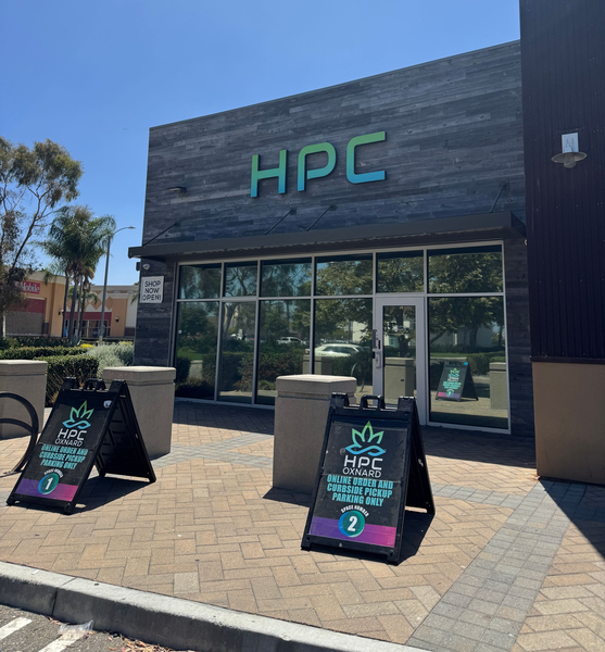 Storefront with green “HPC” sign, glass doors, and two sidewalk chalkboard signs outside.