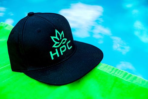 Black HPC cap with neon green logo on a bright green surface against a blue background
