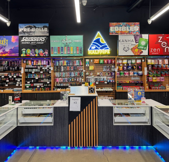 Dispensary interior with shelves of products, neon signs, and two white display under black ceiling lights