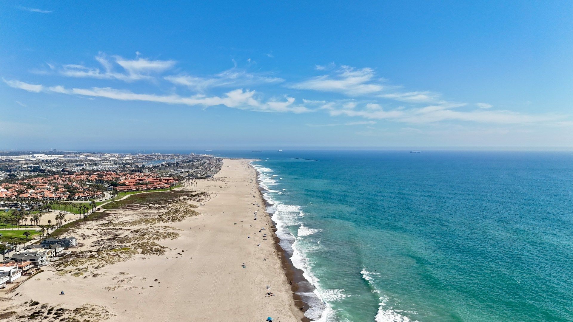 Aerial view of a long sandy beach beside turquoise ocean and a coastal town under a blue sky