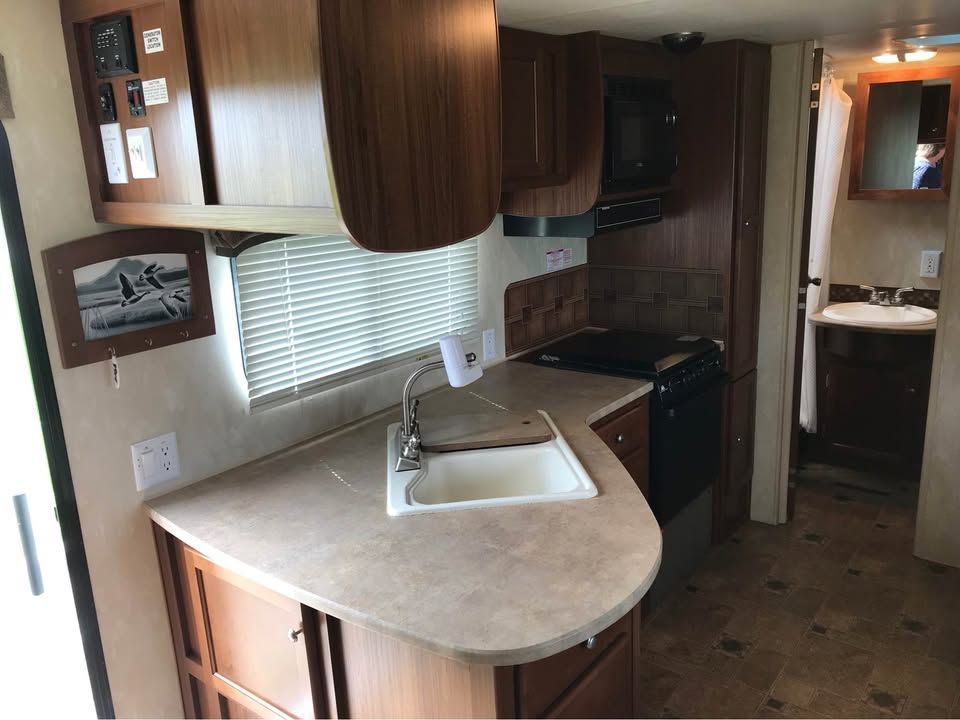 Compact RV kitchen with sink, stove, wood cabinets, and a window with blinds