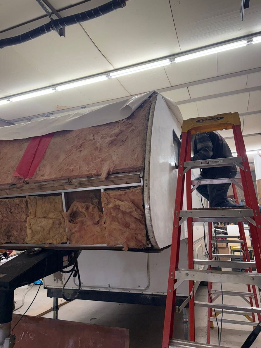 Workers on a red ladder inspecting a large insulated structure in an industrial room.