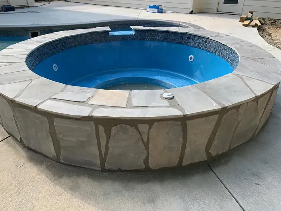 Round stone hot tub or small pool with blue interior on a concrete patio.