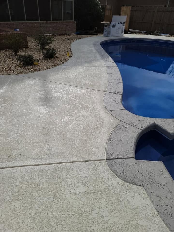 Curved concrete pool deck beside a blue swimming pool and spa, with landscaping in the background