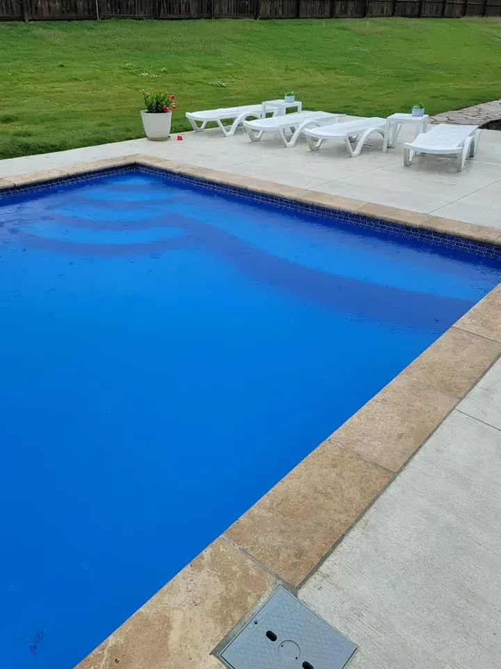 Backyard swimming pool with white lounge chairs and a potted plant on the deck