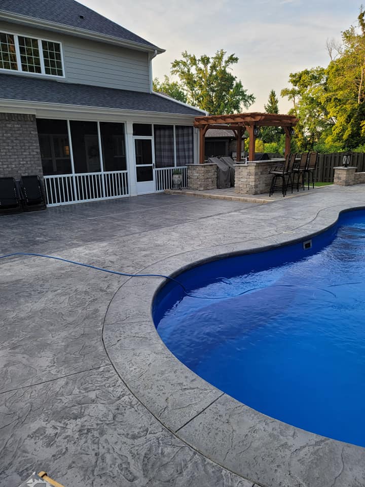 Backyard pool beside a stone patio and house porch at dusk