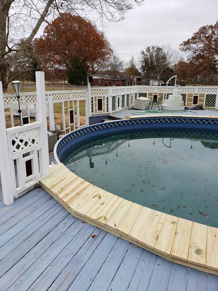 Backyard pool with blue deck boards, white railing, and a wooden ramp over the winter waterline