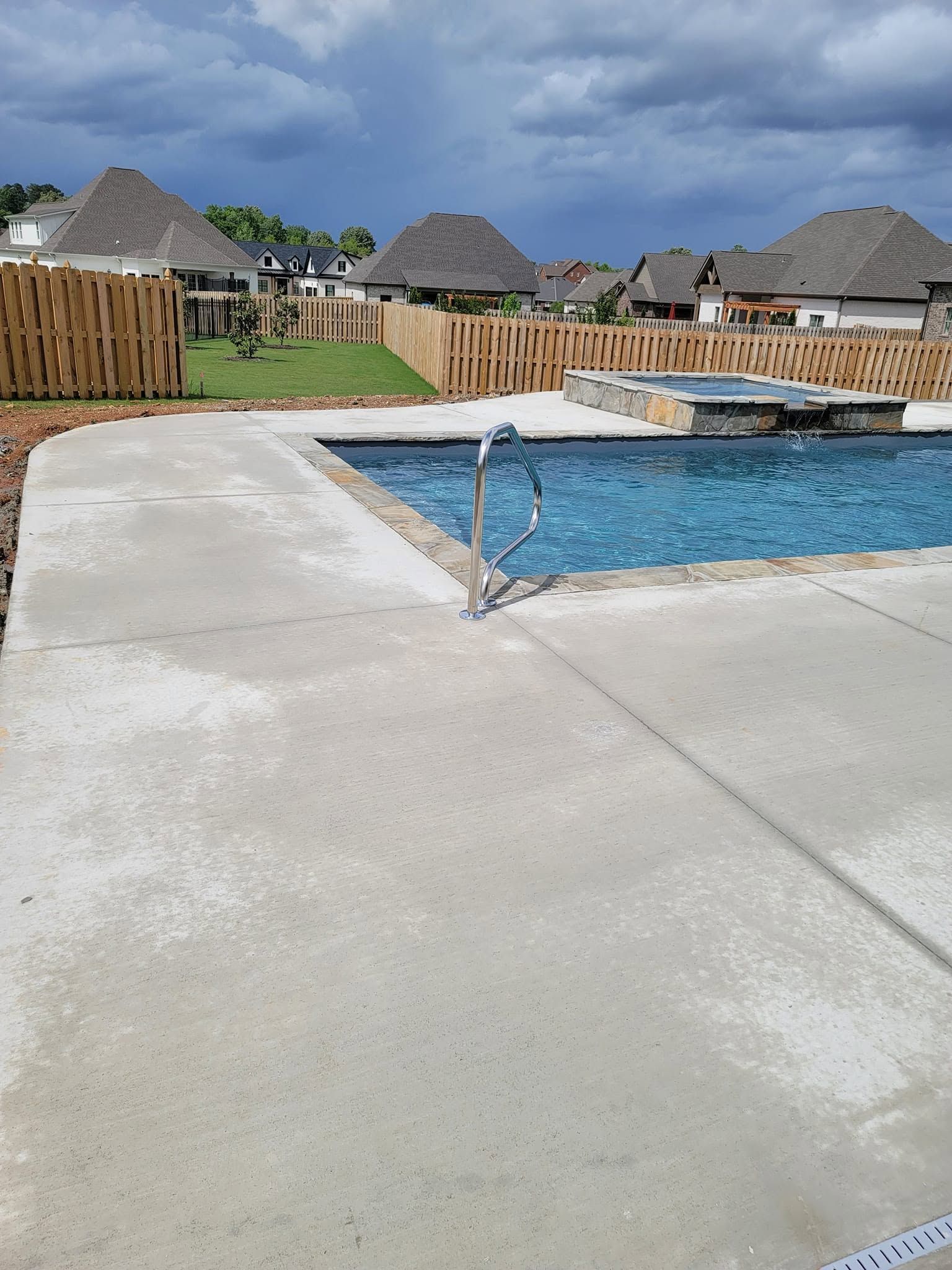 Backyard pool with concrete deck, wooden fence, and thatched-roof huts in the background