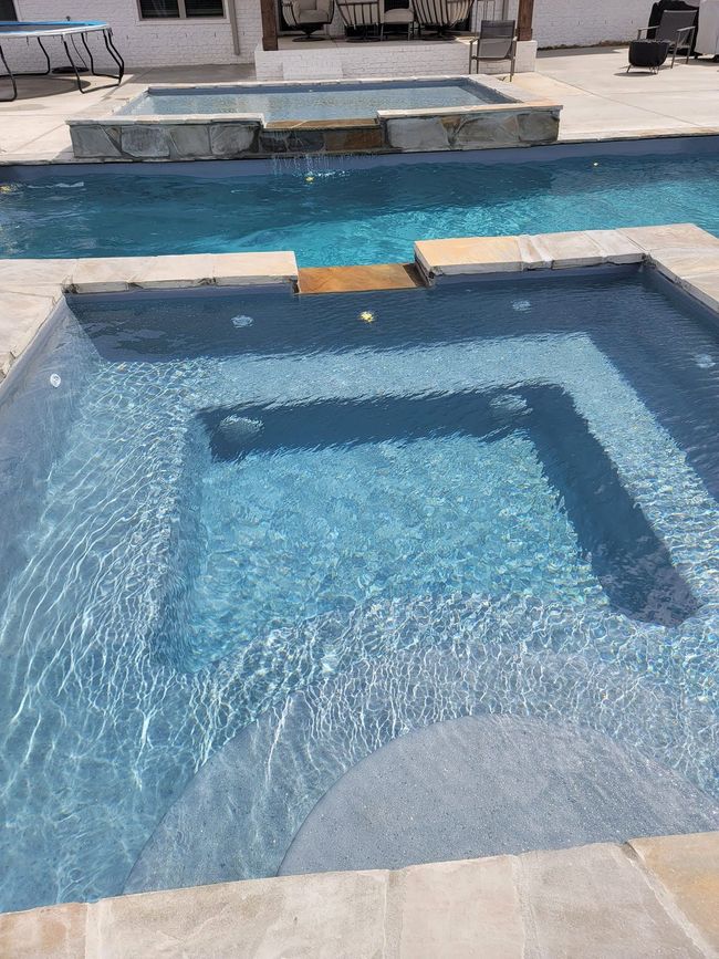 Blue-tiled swimming pool with a raised spa and stone patio in the background