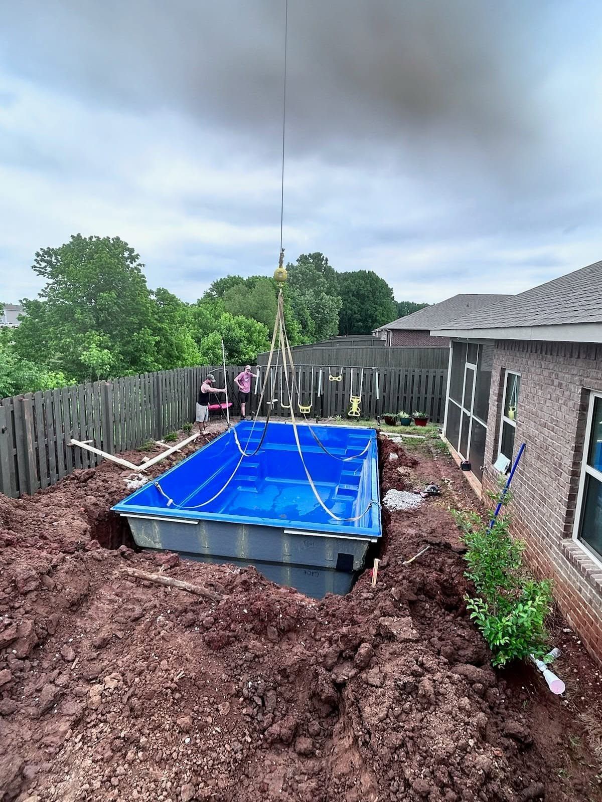 Above-ground pool in a muddy backyard under construction beside a house and fence