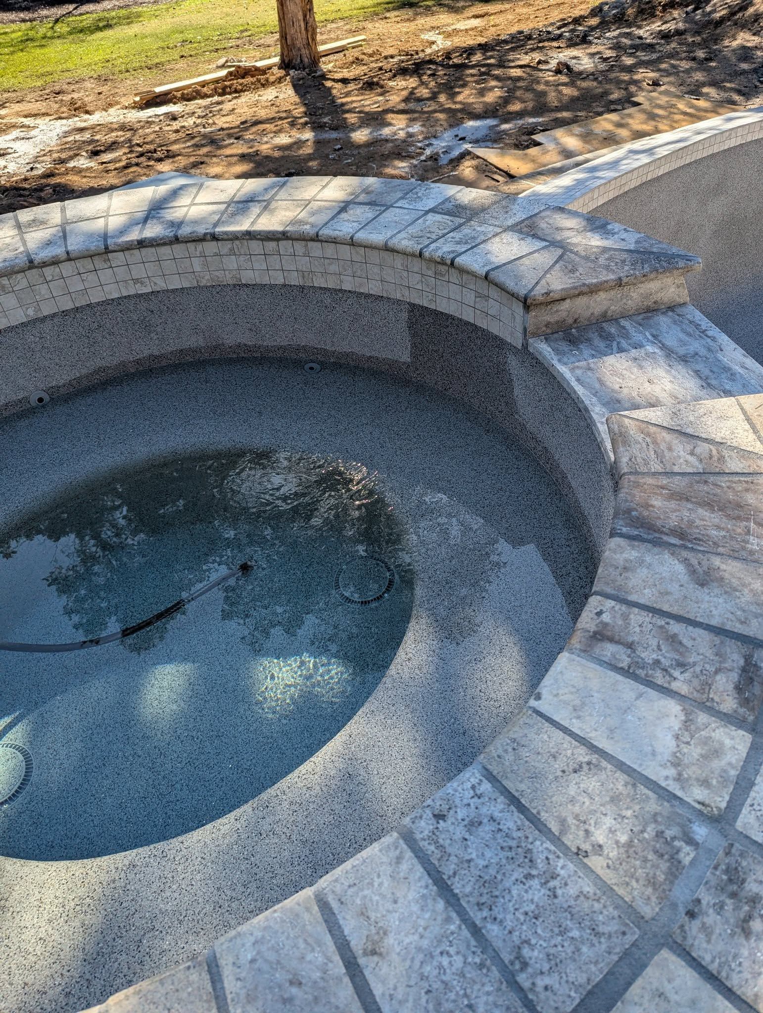 Stone hot tub built into a paved patio, with clear water and a landscaped yard nearby