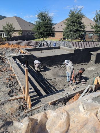 Workers excavating a backyard pool site with concrete walls and a dirt-filled pit, surrounded by houses.