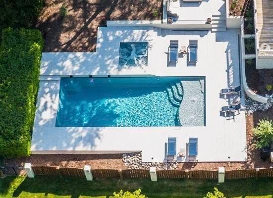 Aerial view of a backyard with a rectangular swimming pool, lounge chairs, and patio seating.