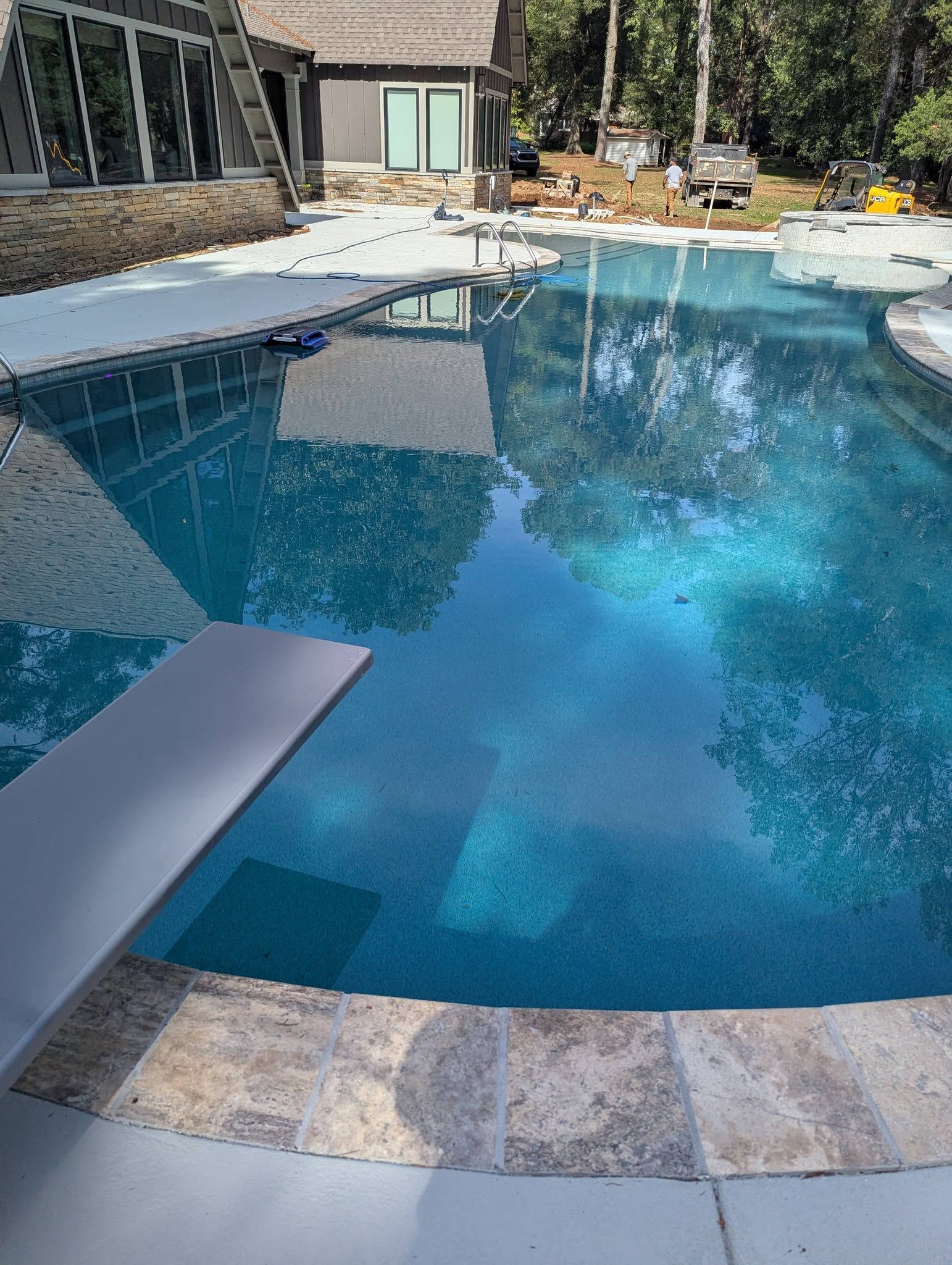 Backyard swimming pool with blue water, stone patio, and lounge chairs by a house