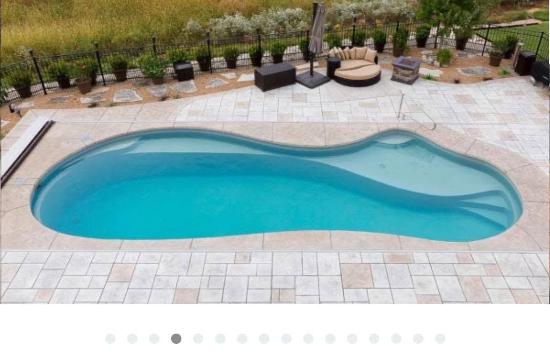 Backyard swimming pool with blue water, paved deck, and lounge chairs in a landscaped yard