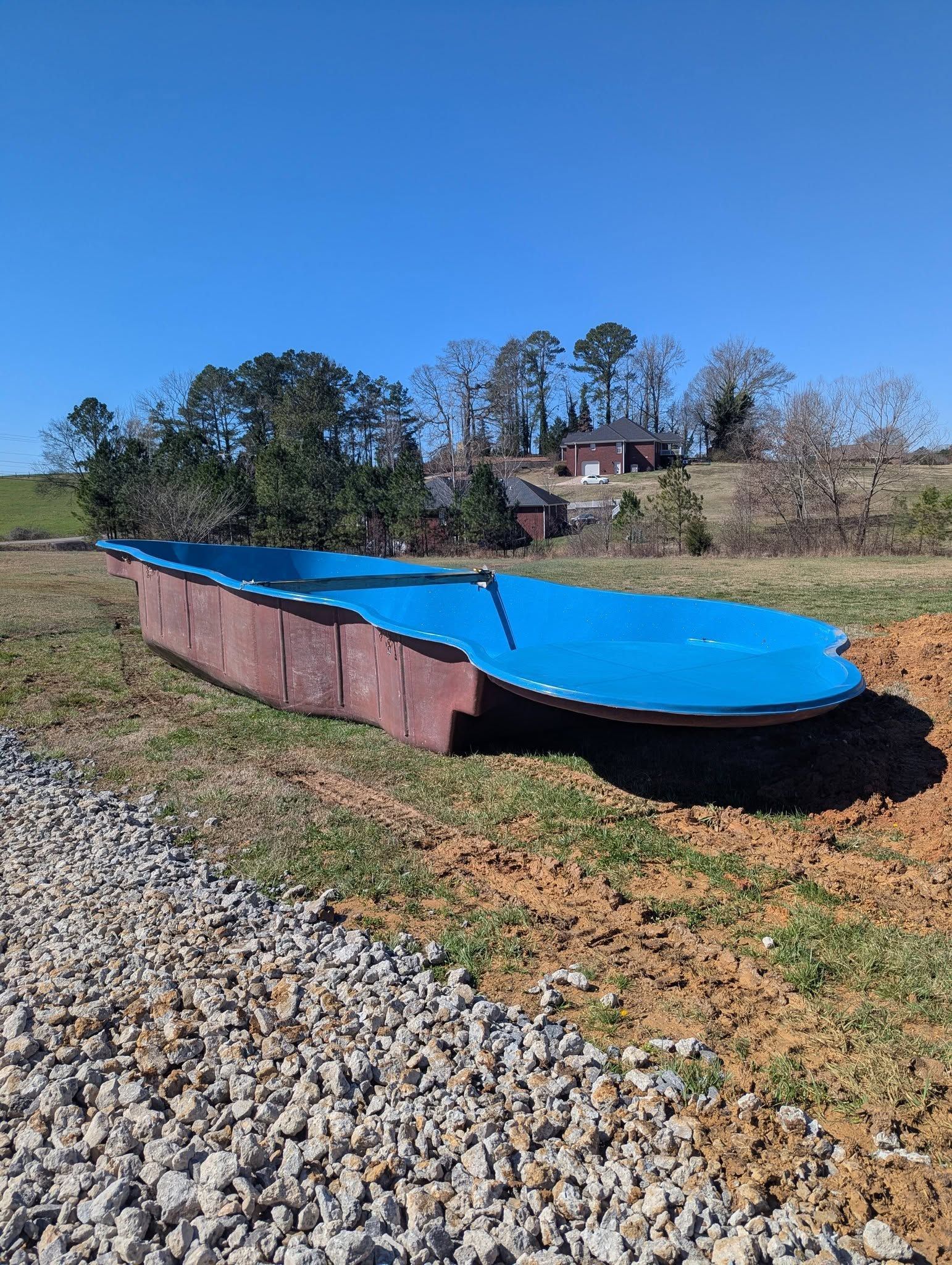 Blue covered saltwater pool beside a gravel path on a sunny hillside.