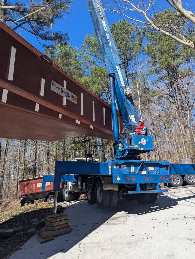 Blue crane lifting a large steel beam in a wooded construction site