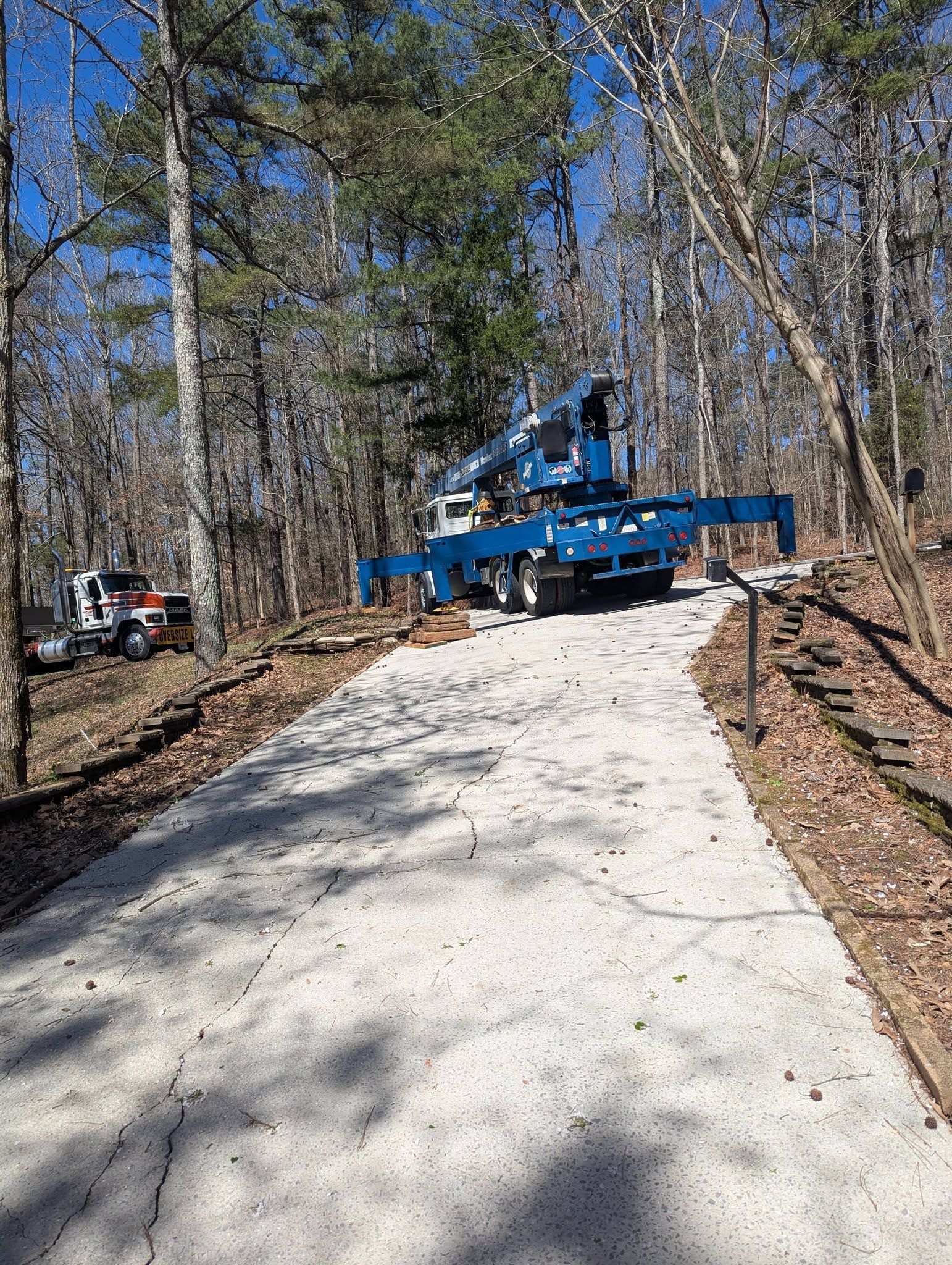 Blue utility truck on a gravel path in a wooded area, with a white vehicle off to the left.